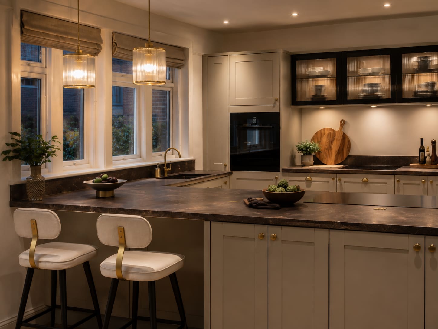 Warm-toned bespoke kitchen with dark stone worktops and brass pendants